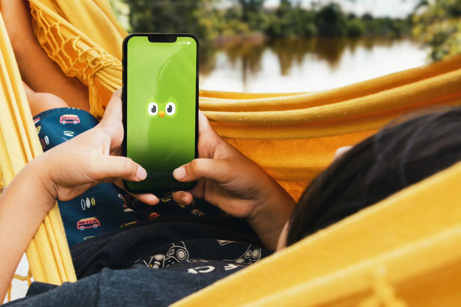 Kid in hammock with duolingo on a phone screen