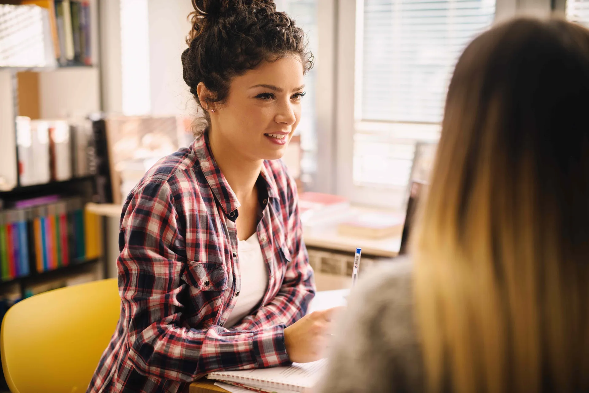 A young woman in a library is smiling at another woman off camera.