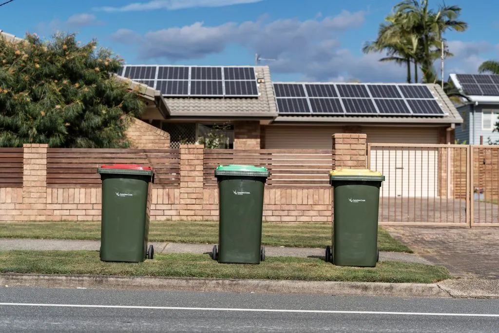 Three bins sit on the nature strip in front of a house, awaiting collection.