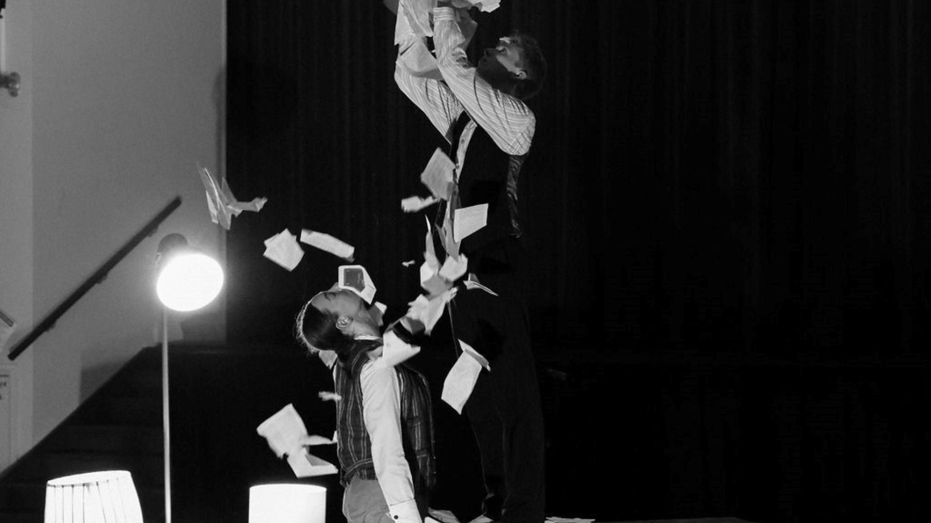 Labyrinth performance. Two dance actors, one standing on a chair with papers flying in the air