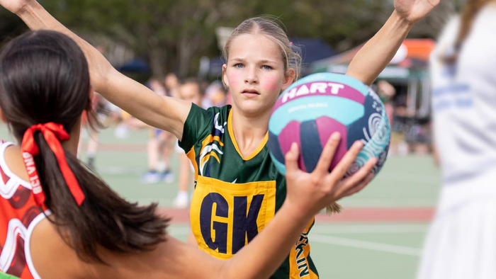 Two young netballers one attempting to pass the ball, another with arms out stretched to block the pass.