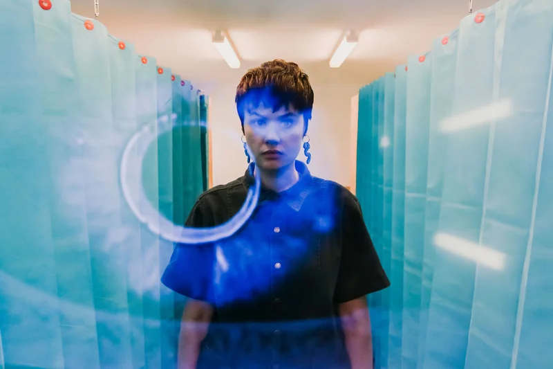 A lady facing the camera standing in between two hospital curtains