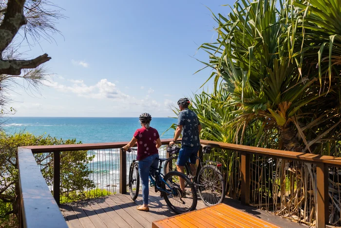 Two people on bikes watch the ocean from a lookout at Moffat Beach headland.