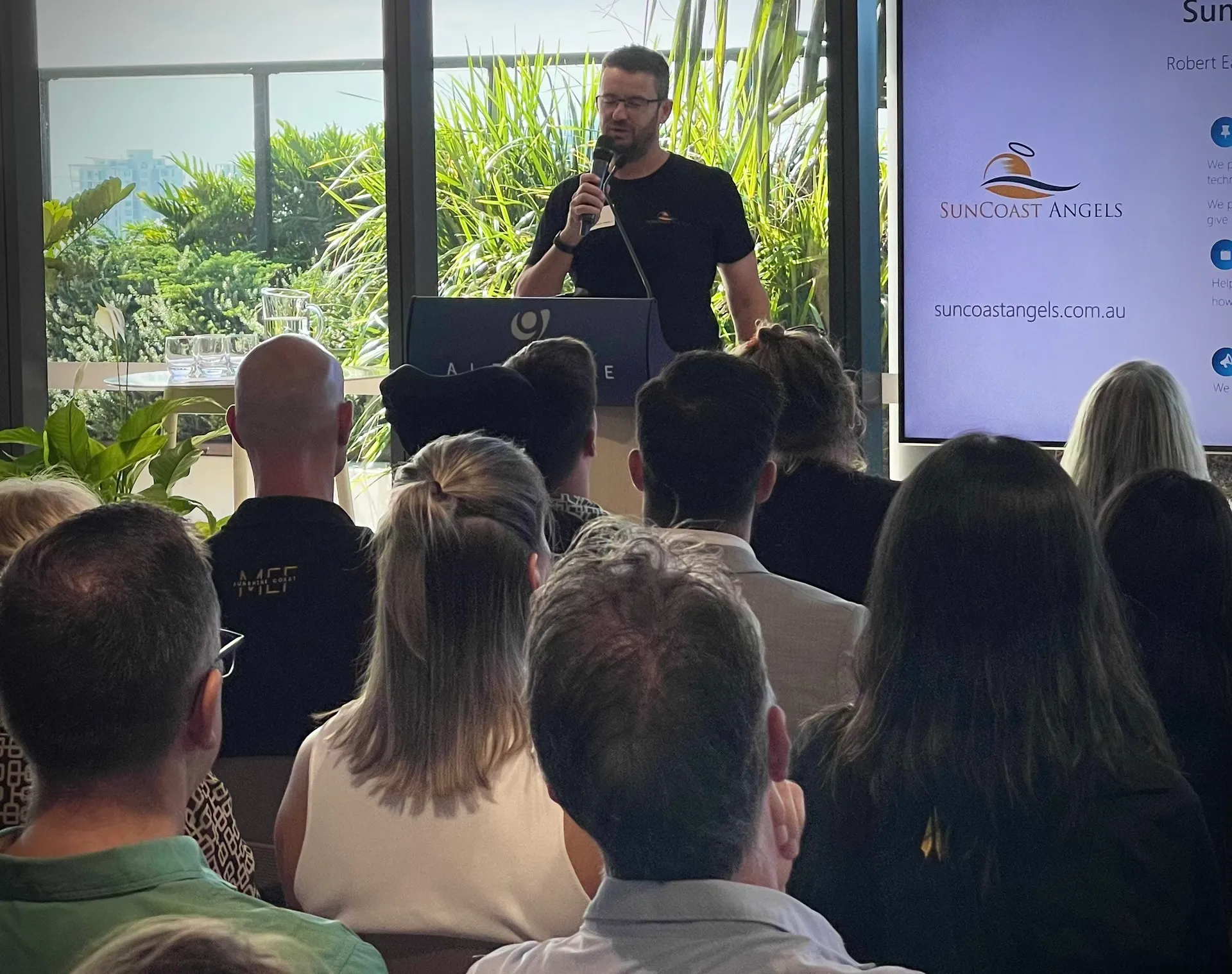 A man stands behind a podium talking to a room full of people seated.