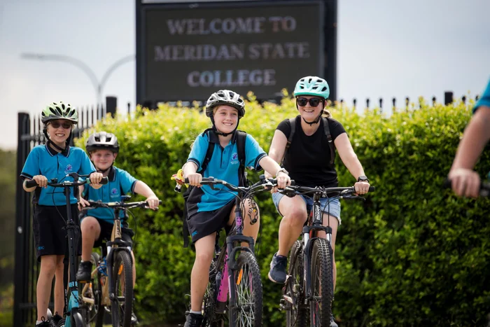 Group of school students smiling while riding their bikes to school. 