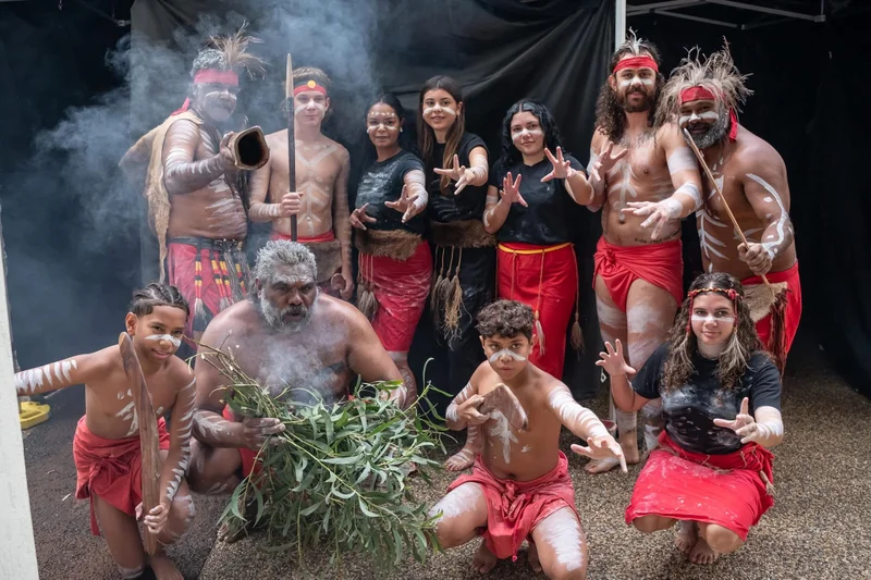 Local First Nations performers at Council's 2024 NAIDOC Flag Raising event. Dressed in traditional attire are men and women, boys and girls of all ages posing with arms out to camera.