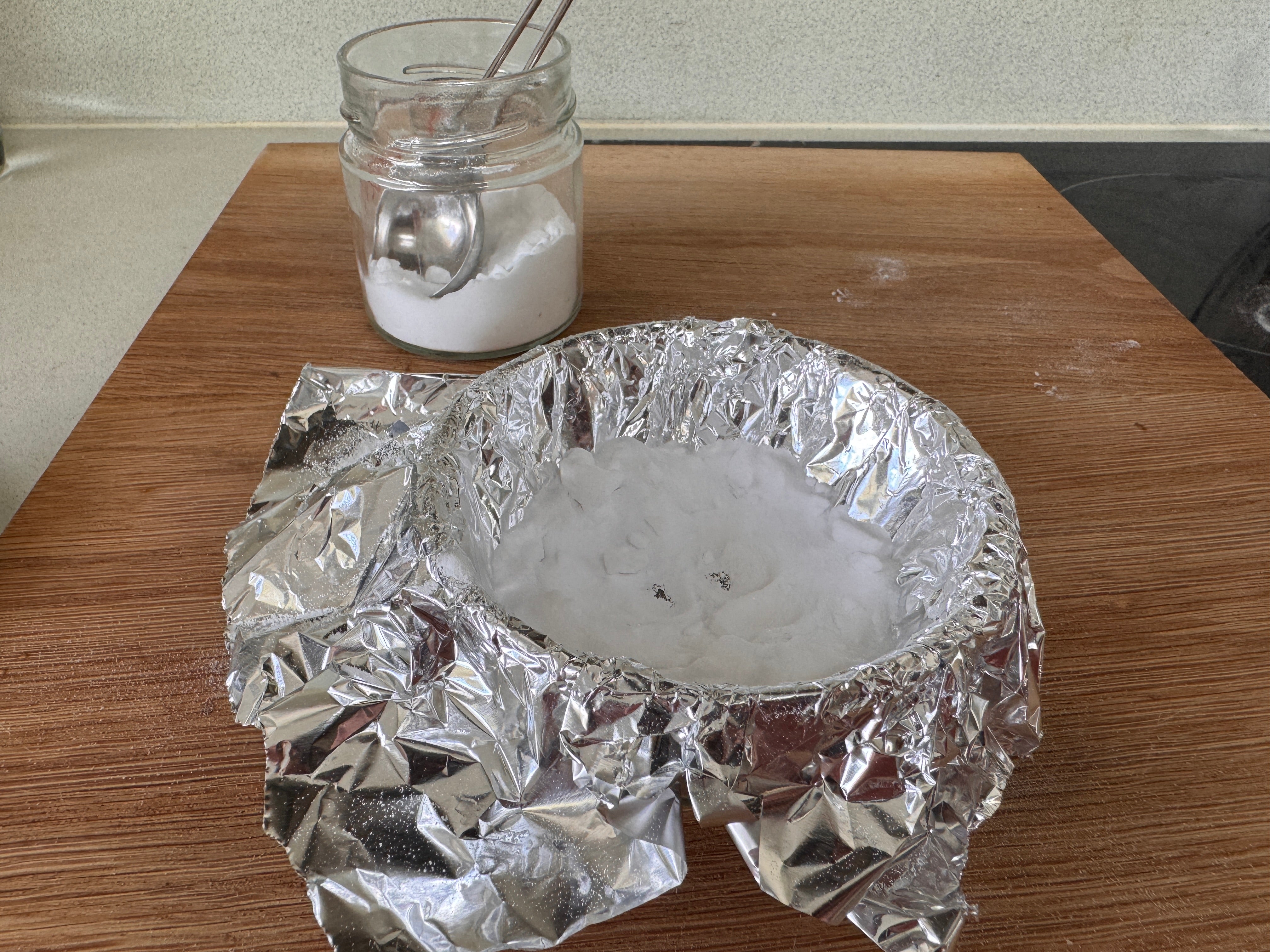 tin foil lined glass bowl containing a silver bangle covered in baking soda