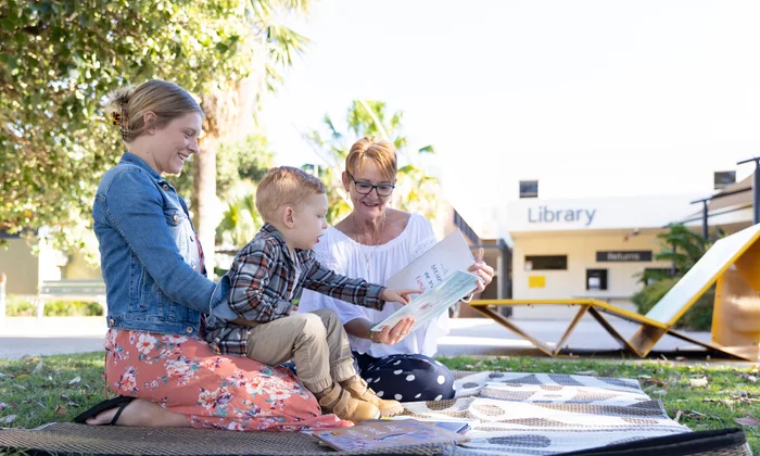 Family reading a picture book to a young child outside Maroochydore Library.