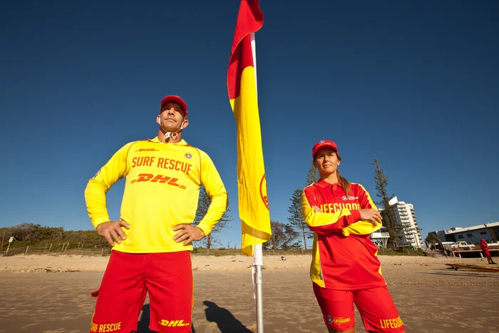 Two lifeguards looking out to sea, with a red and yellow beach safety flag in between them.
