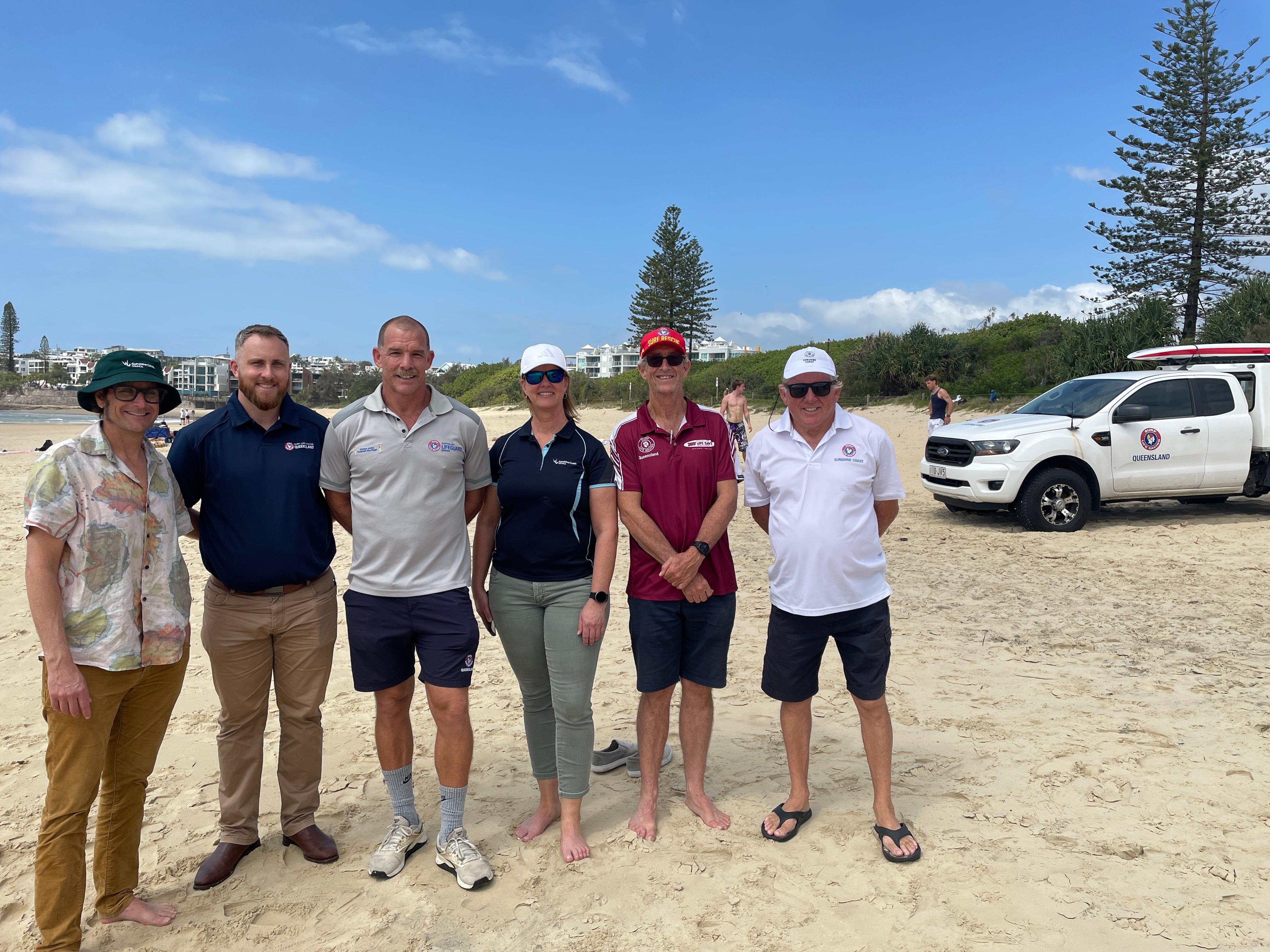 People standing on the beach with a Surf Life Saving vehicle to the right. Cr Tim Burns, SLSQ Aaron Purchase and Trent Robinson, Cr Maria Suarez, Gerard O'Brien President SLSQ and Tim Ryan President SLSQ - Sunshine Coast Branch (P)