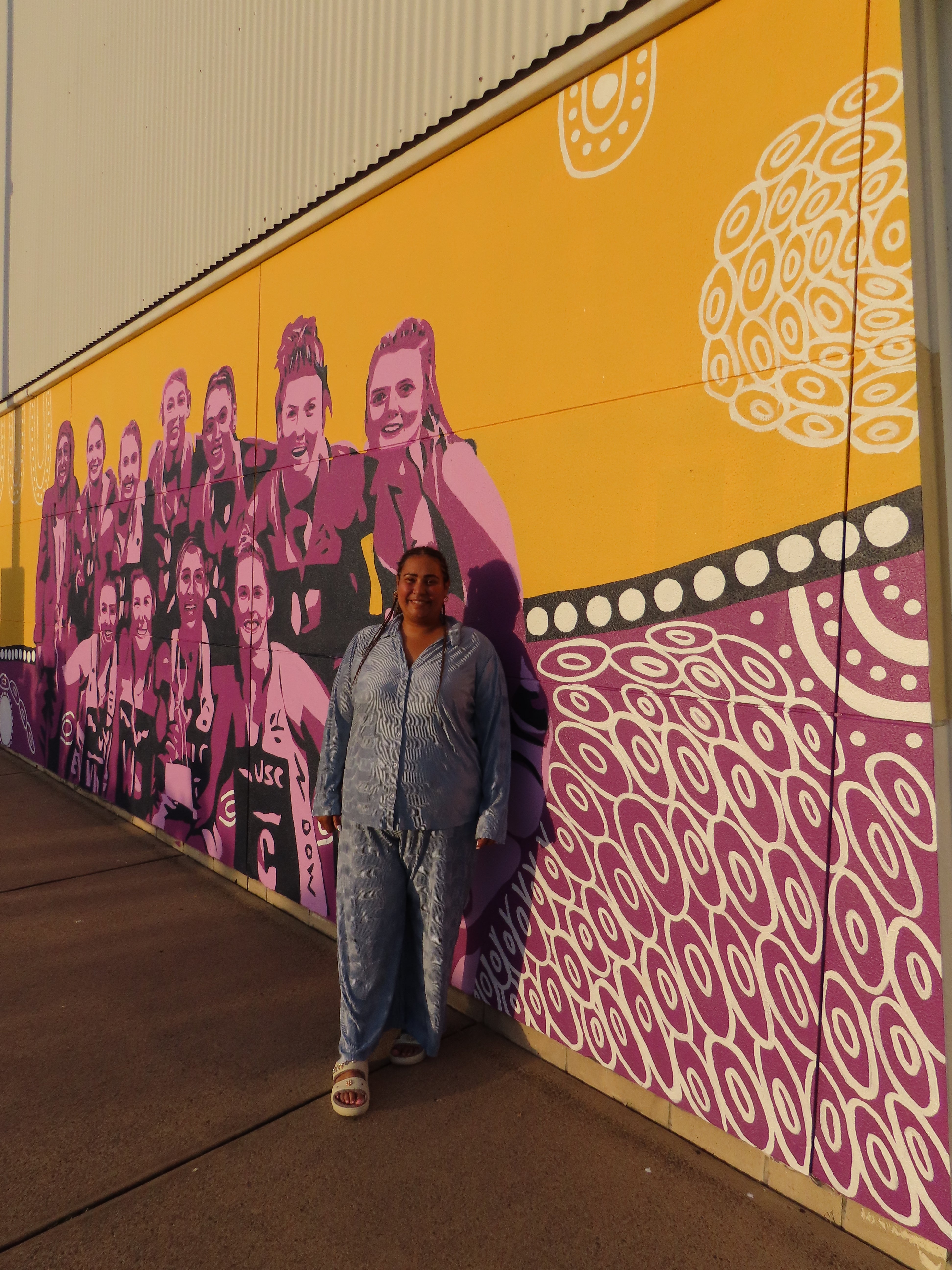 First Nations Artist Zartish Davis with her artwork on display at Caloundra Indoor Stadium for the Sunshine Coast Lightning mural.