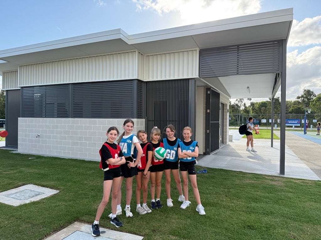 Young girls playing netball, with new Play Our Way amenities in the background, Caloundra Indoor Sports Complex