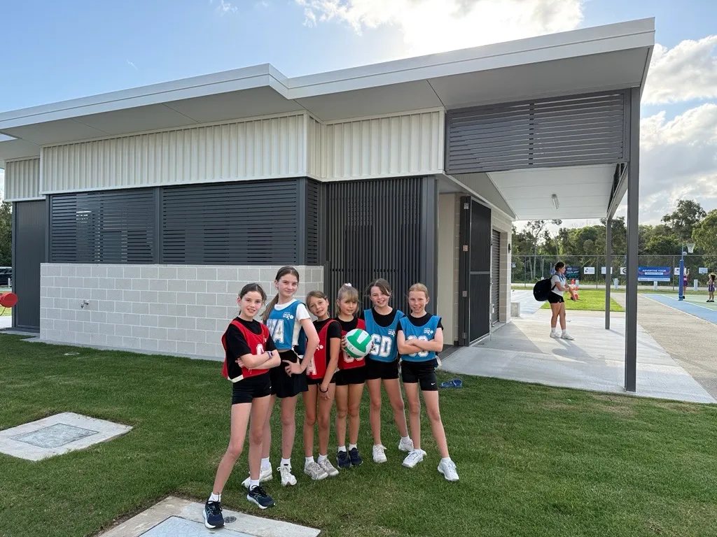 Young girls playing netball, with new Play Our Way amenities in the background, Caloundra Indoor Sports Complex