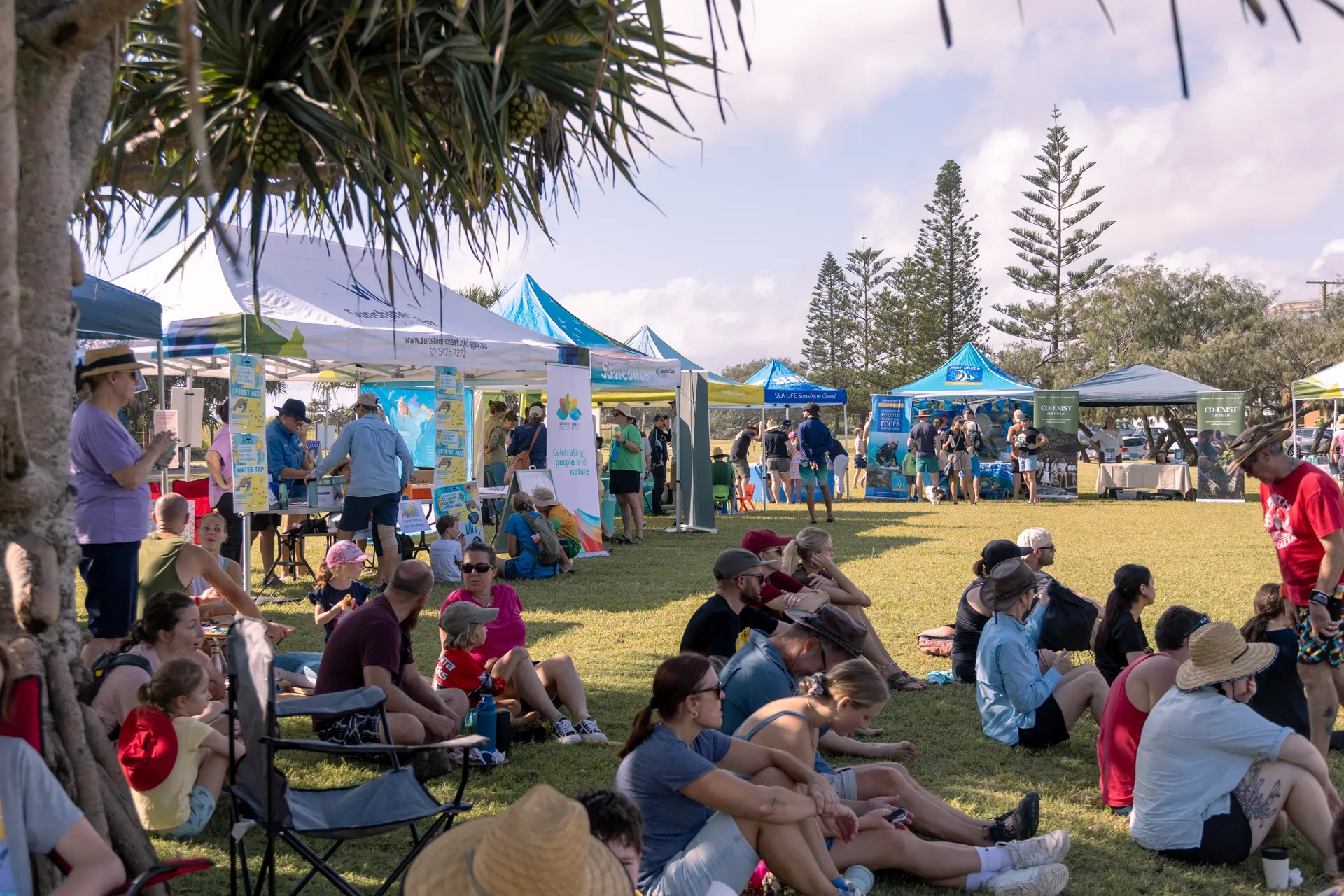 A group of people seated on grass around education stalls at the Clean up for the hatchlings thank you event.