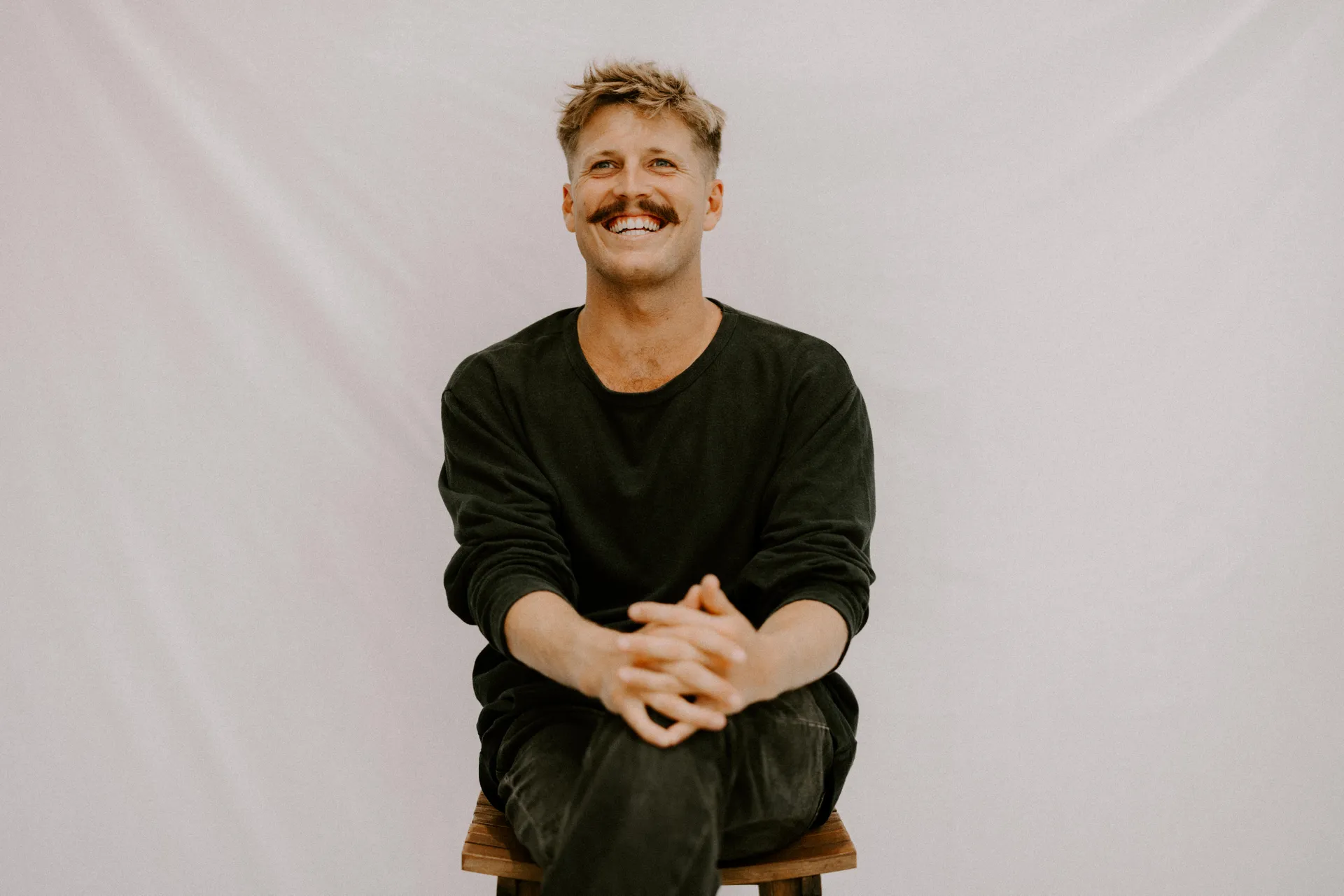 Musician Ziggy Alberts - sitting on a stool with this hands clasped on his knees