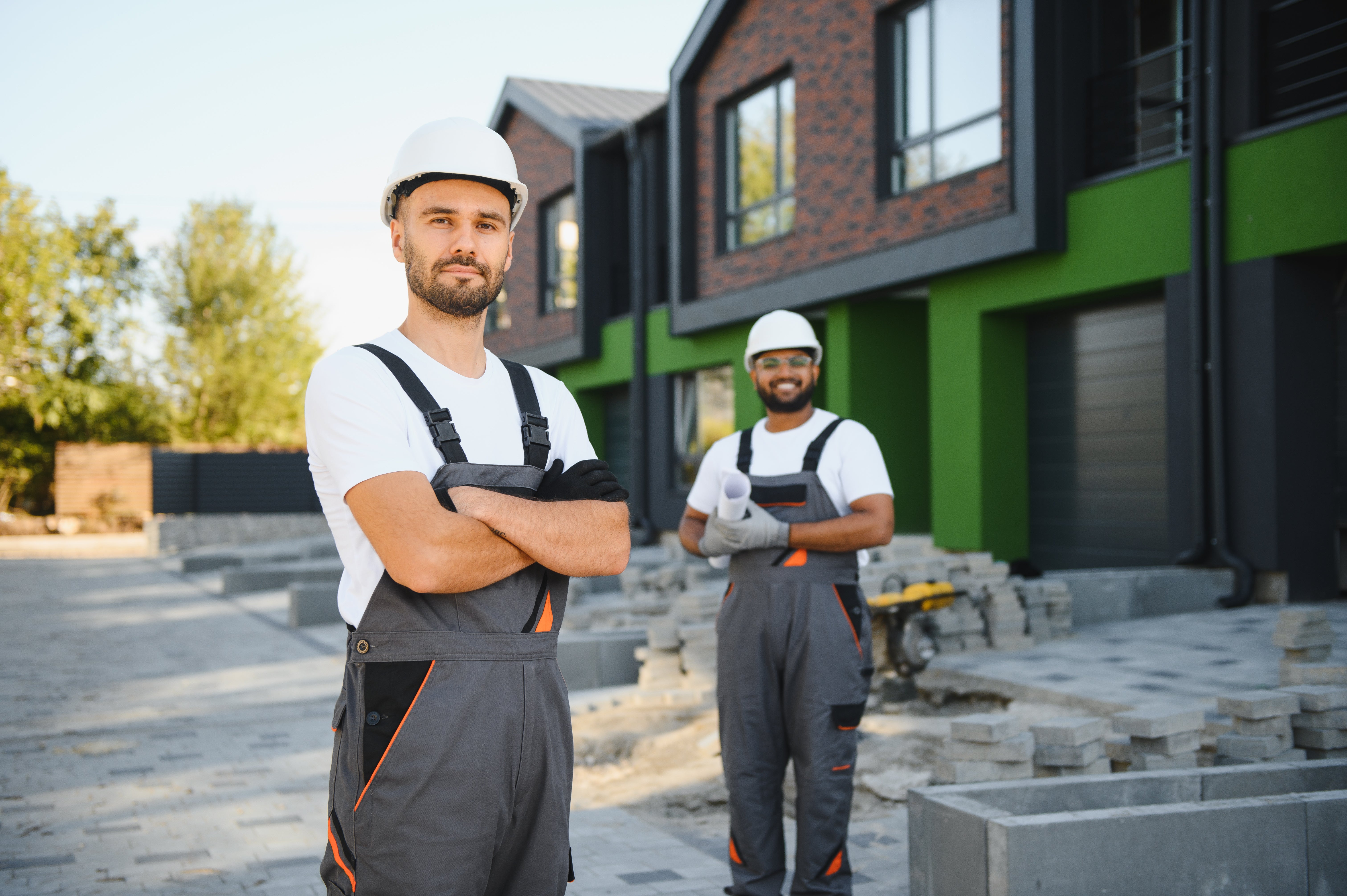 two builders in hard hats and overalls outside a building project