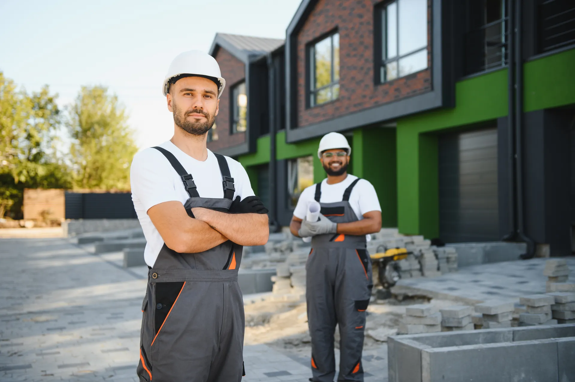 two builders in hard hats and overalls outside a building project