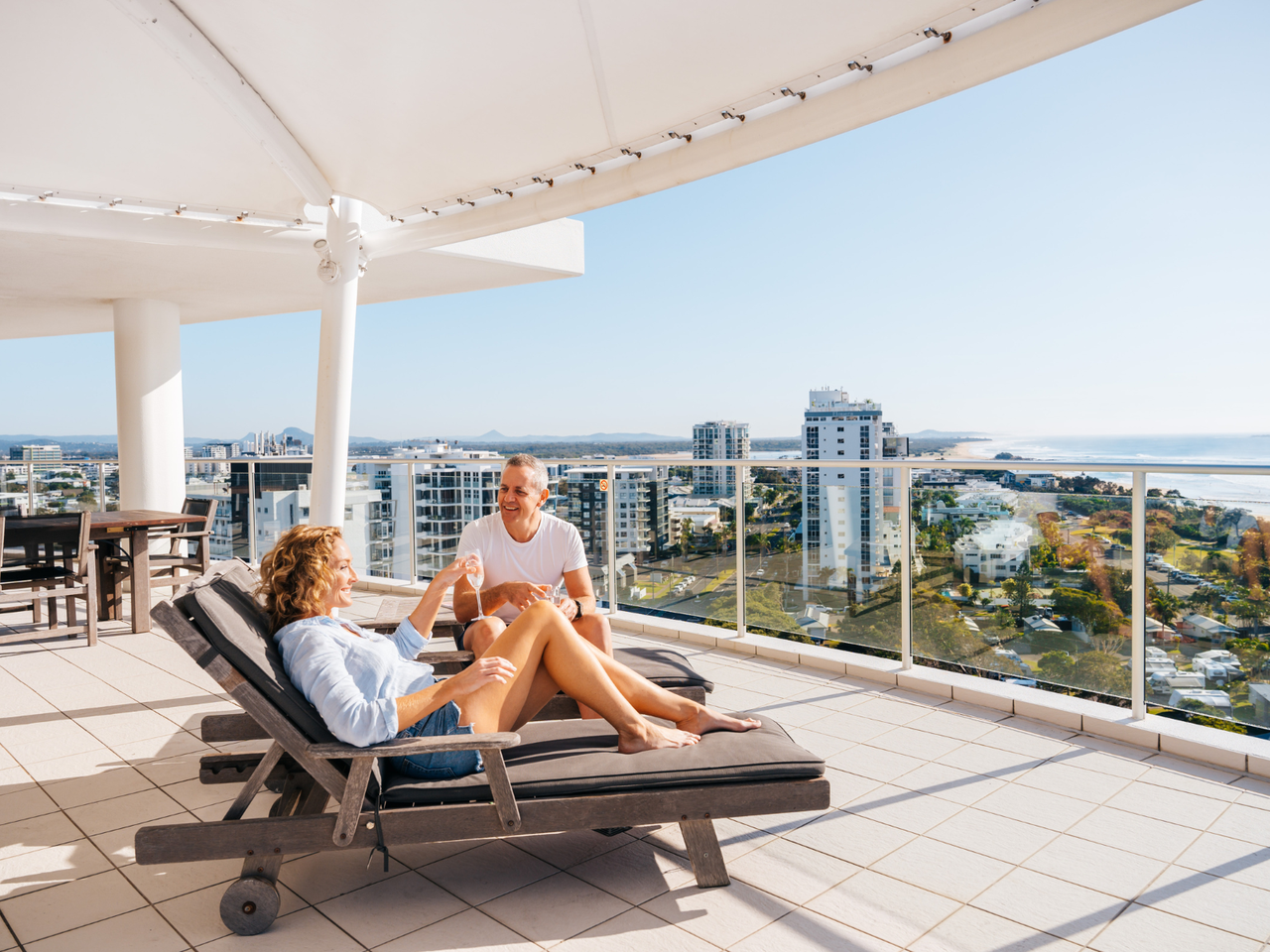 Hotel balcony with people sitting/lying on deck chairs enjoying the view