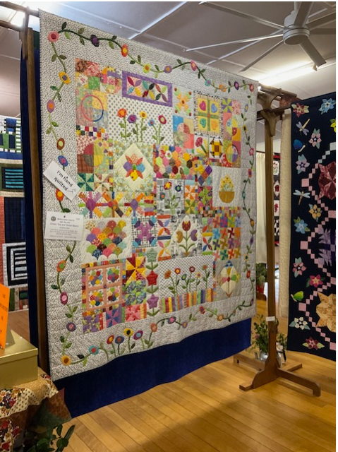 Intricate patchwork quilit wiht orange, purple flowers, hearts and carefully stitched artwork. 