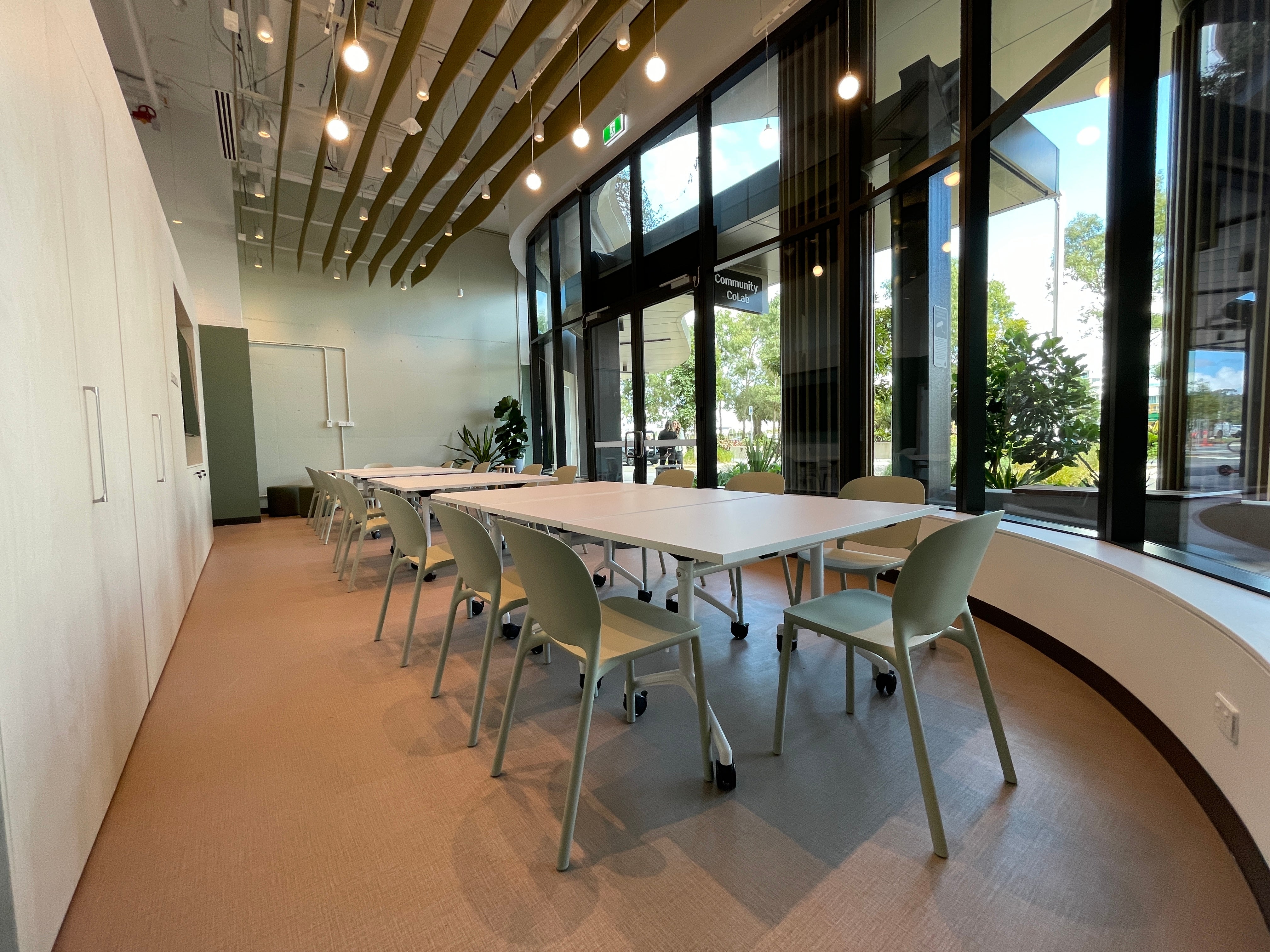Image shows inside space of Community CoLab, featuring a long white table surrounded by white chairs.