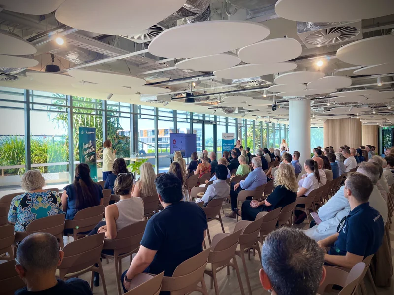 A light-filled room filled with people seated and facing two women standing at the front.