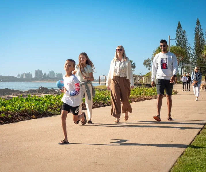 "Adults and two children walking along a walkway with the ocean in the background."