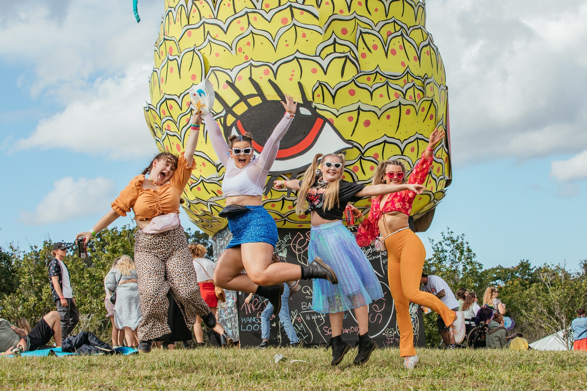 Four festival lovers jumping up in from the Big Pineapple blow up decor 