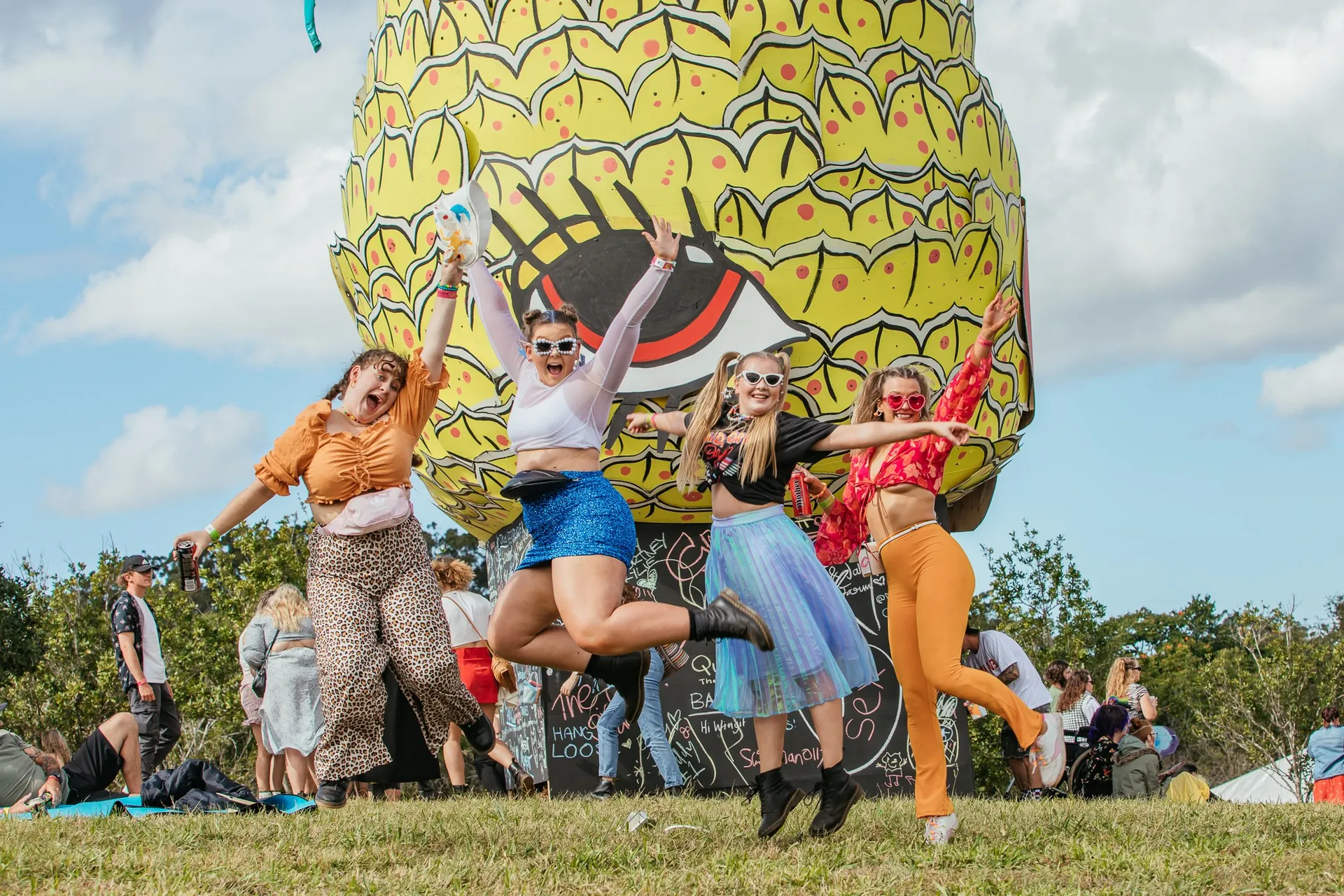 Four festival lovers jumping up in from the Big Pineapple blow up decor
