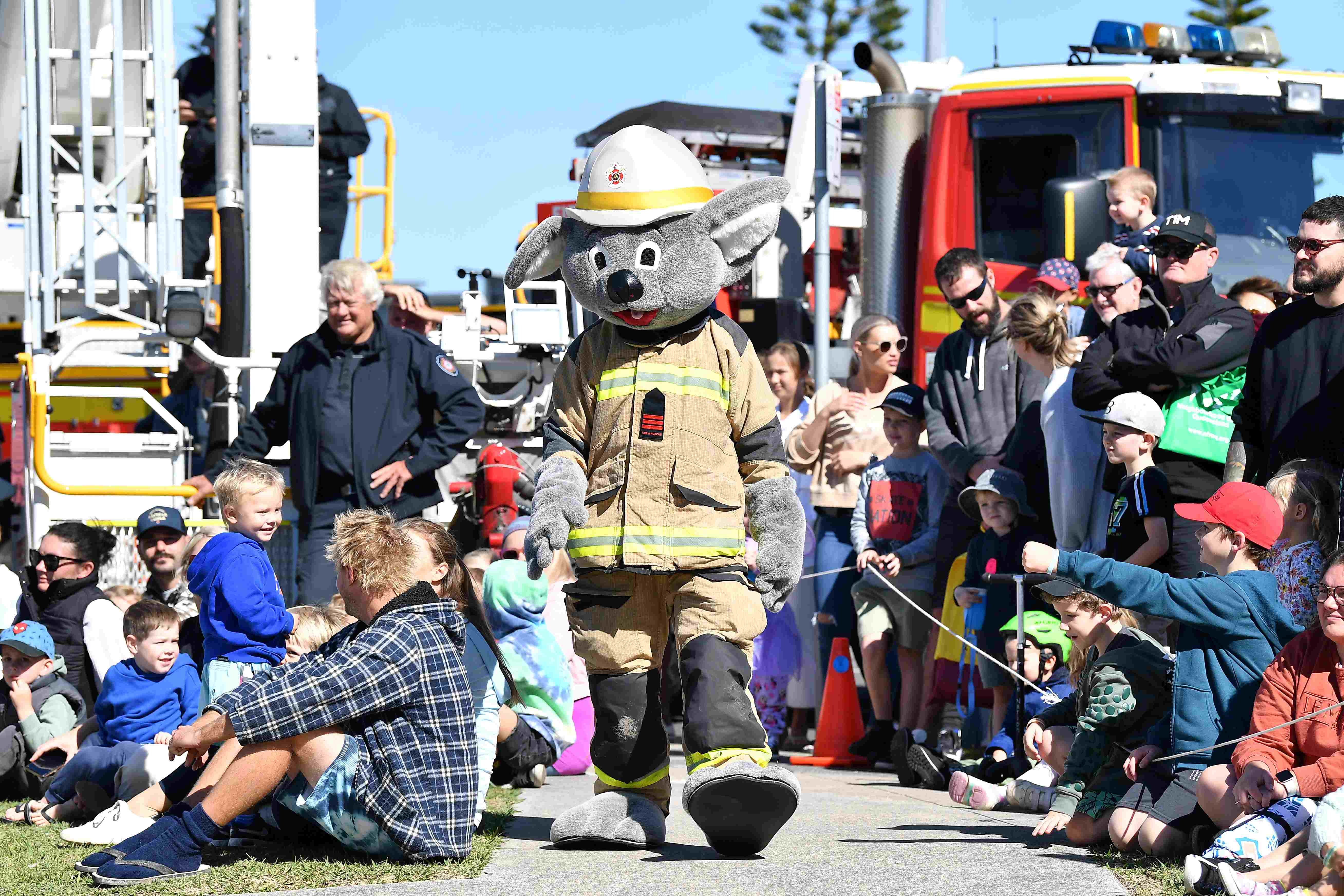 A Koala fire fighter mascot walks through a crowd during a demonstration.