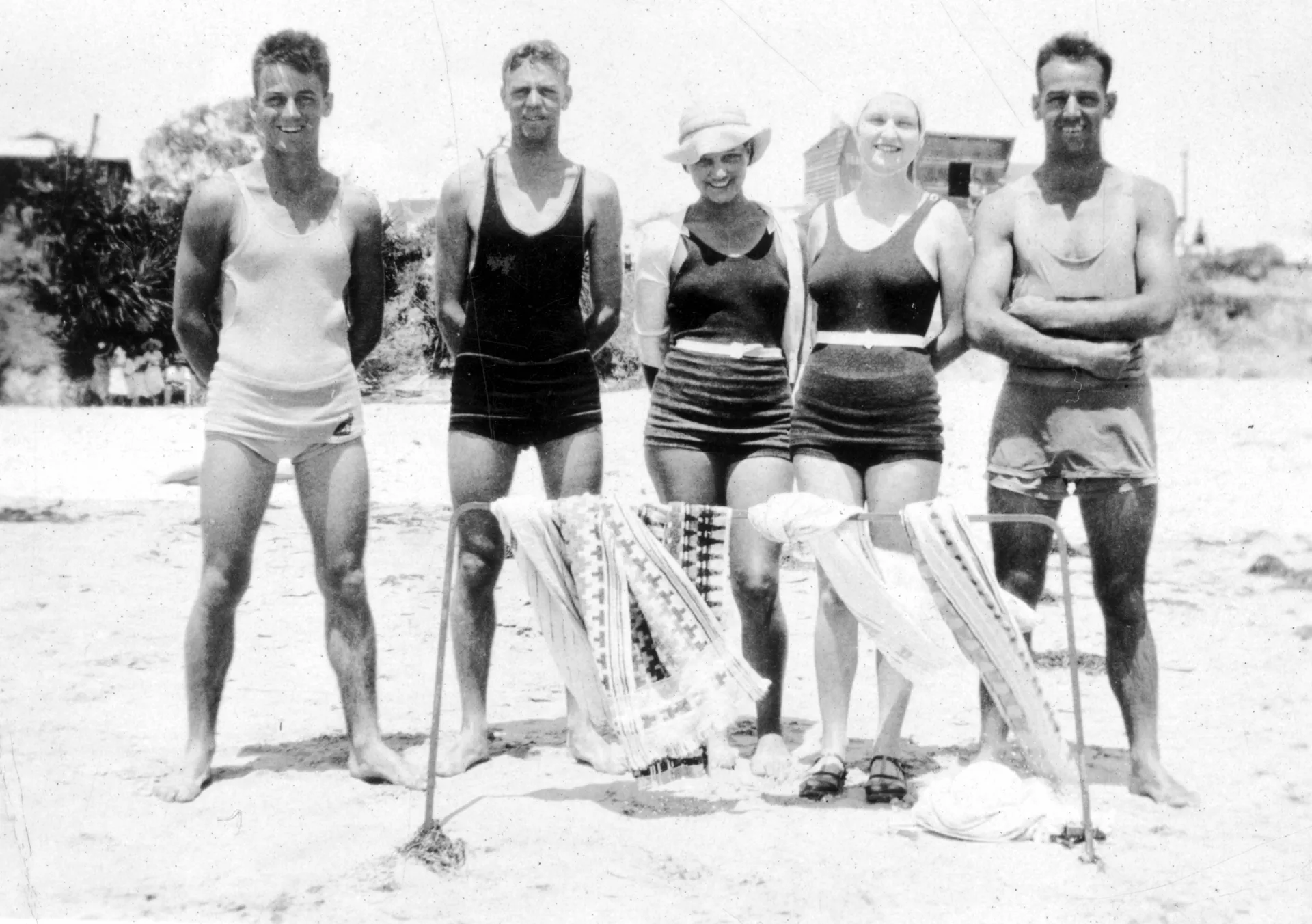 Beachgoers in 1932 captured in a black and white photo. Group of five, three men in tank singlet tops and trunks and women in one-piece bathers.