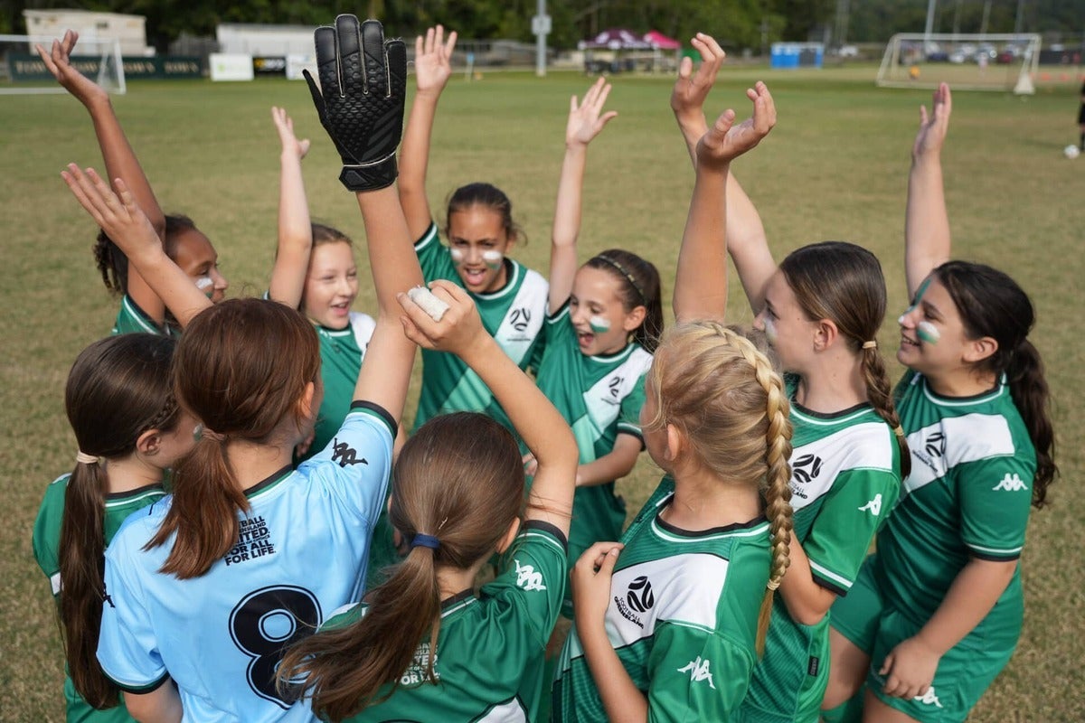 A group of young football players with their hands up in the air building team spirit.