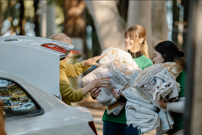 two ladies collecting bundles of sheets from the back of a ladies car