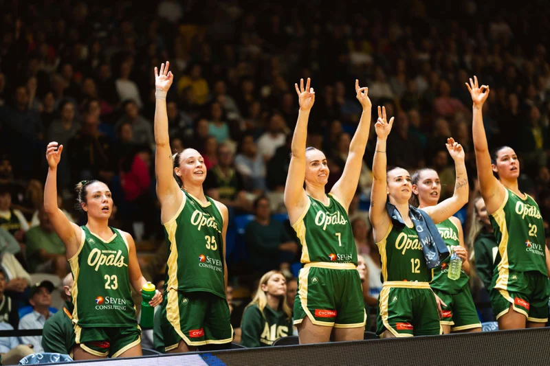 Six Australian Opal basketball players with their hands up in the air cheering their win.