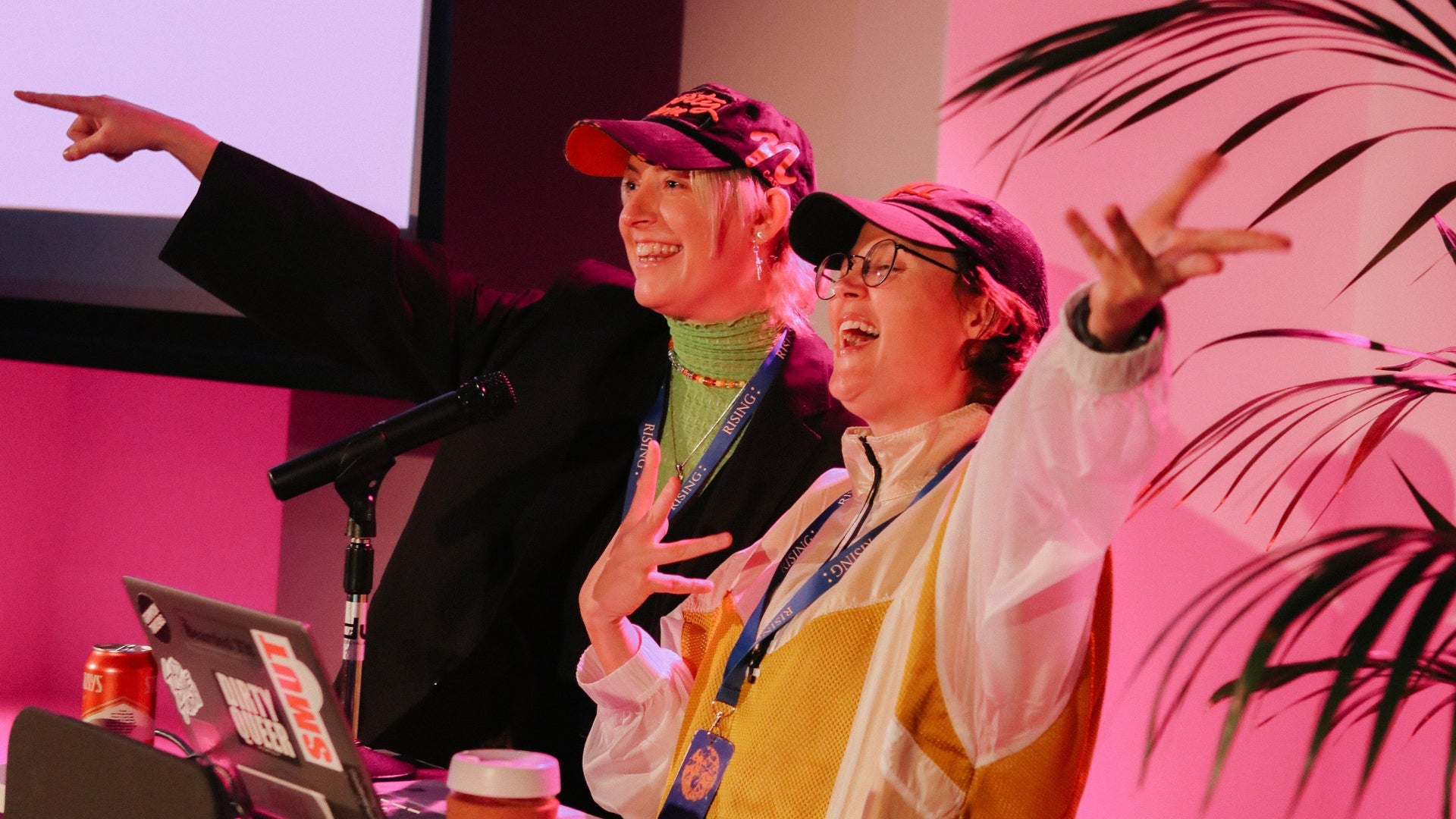 Two people in front of computer and microphone, with hands in the air in joyous rapture.