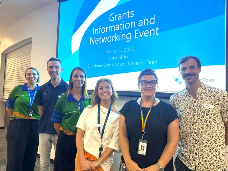 Six smiling people are smiling at the camera while standing in front of a large screen that says Grants Information and Networking Event.