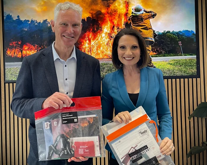 Noosa Mayor Frank Wilkie stands on the left with Sunshine Coast Mayor Rosanna Natoli on the right, in front of a picture of a bushfire. They are both holding their Council's Disaster packs.