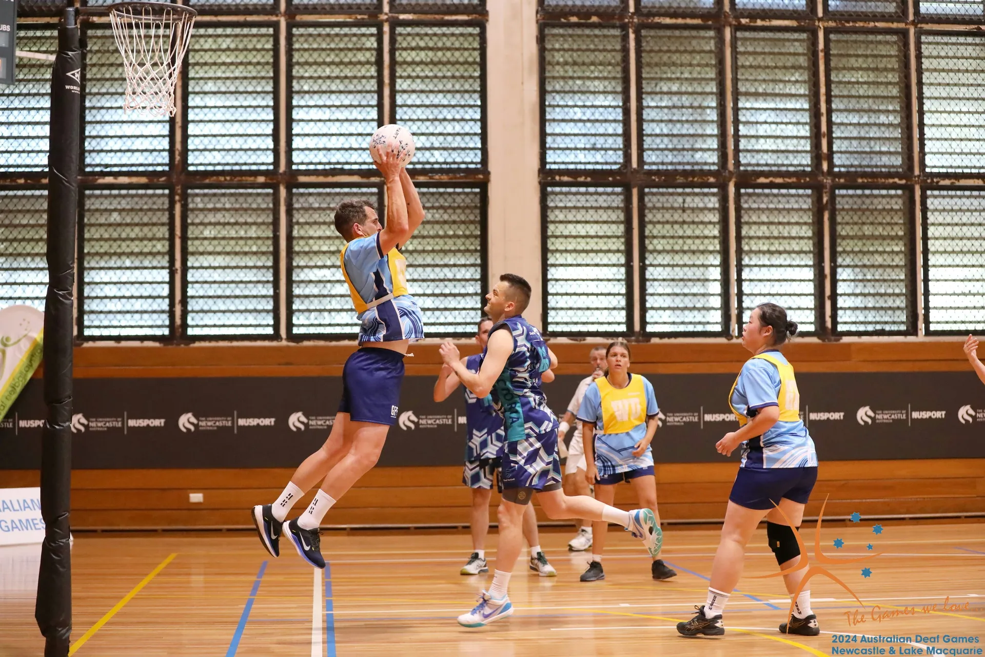 Deaf basketball mixed players on court, with one person jumping up high holding the ball about to pass it.