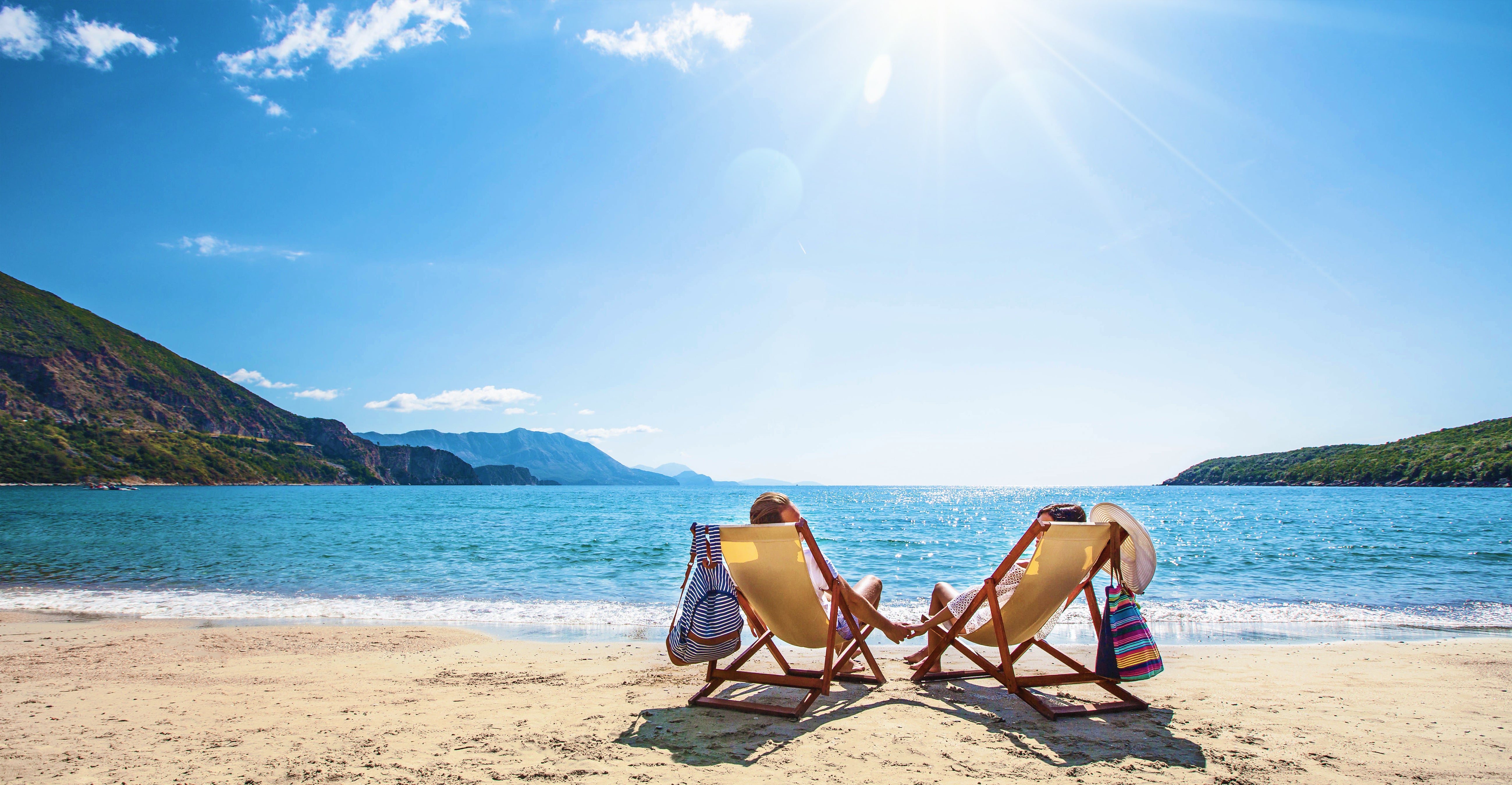 a sunny beach, two deckchairs and a couple sitting in them holding hands