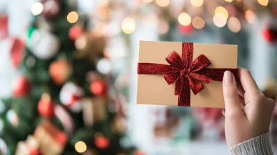 hand holding a festive envelope in front of a Christmas tree