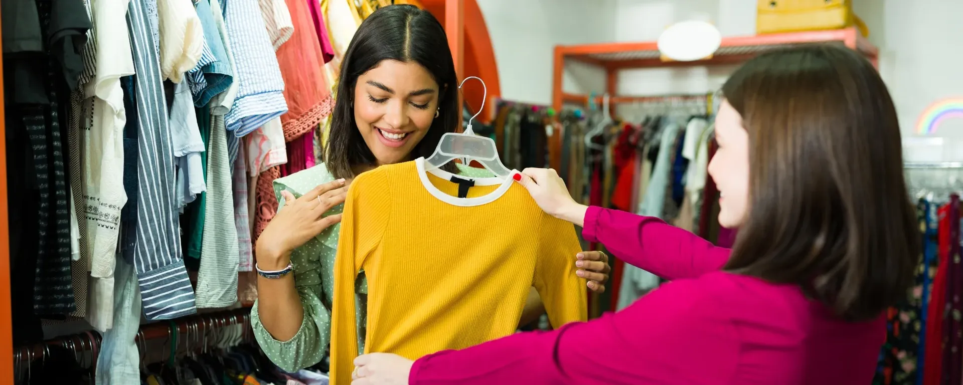 two women looking at a long sleeve yellow top in a charity shop