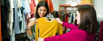 two women looking at a long sleeve yellow top in a charity shop