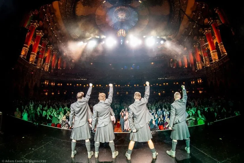 Taken from behind, looking towards the audience, four performers with their right hands up in the air!