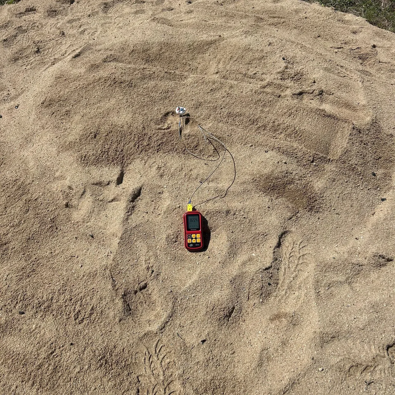 pit dug onto beach showing a temperature gauge in the centre