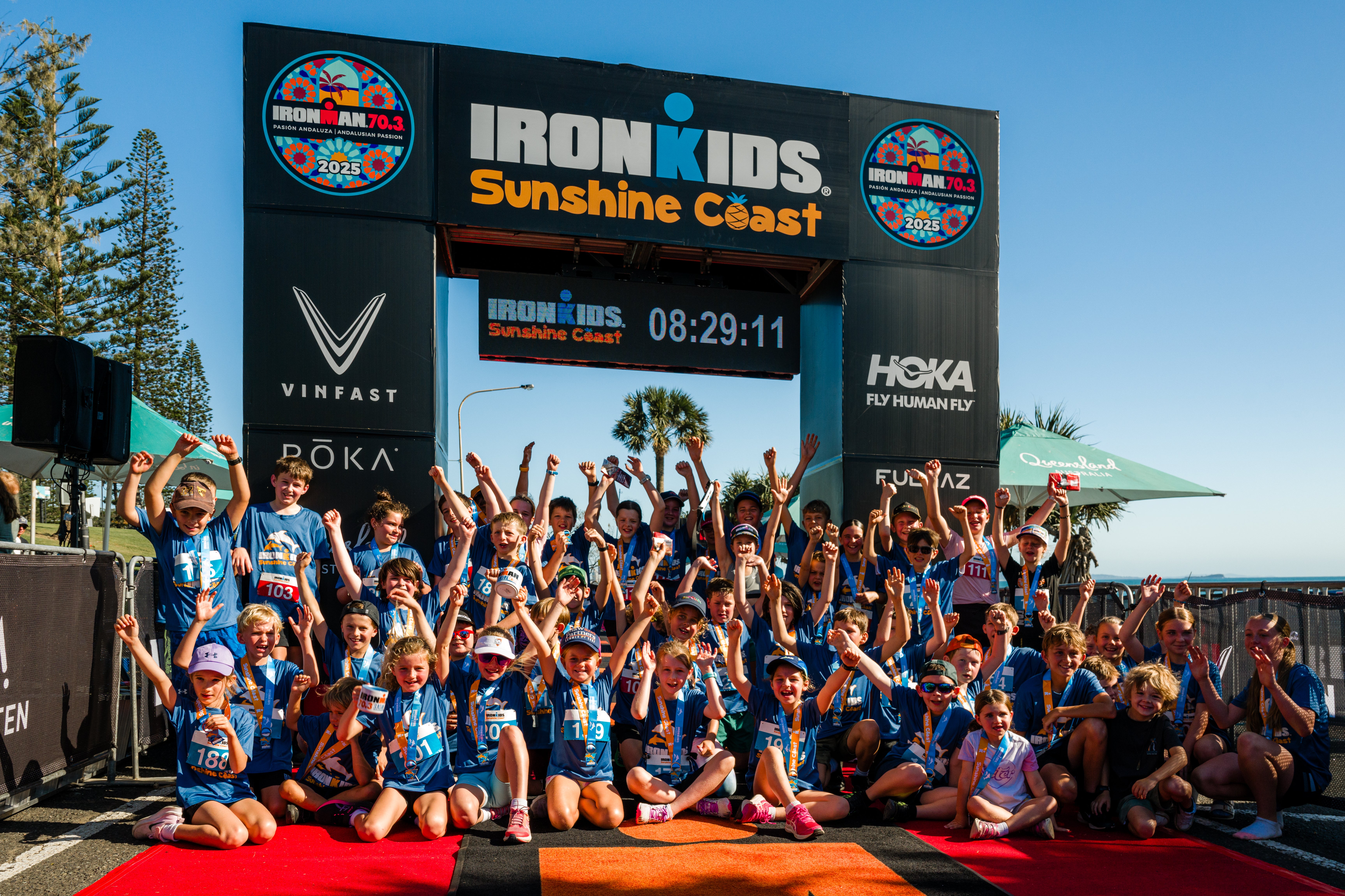 A group picture of IRONMAN kids at the finish line with their arms up in the air!