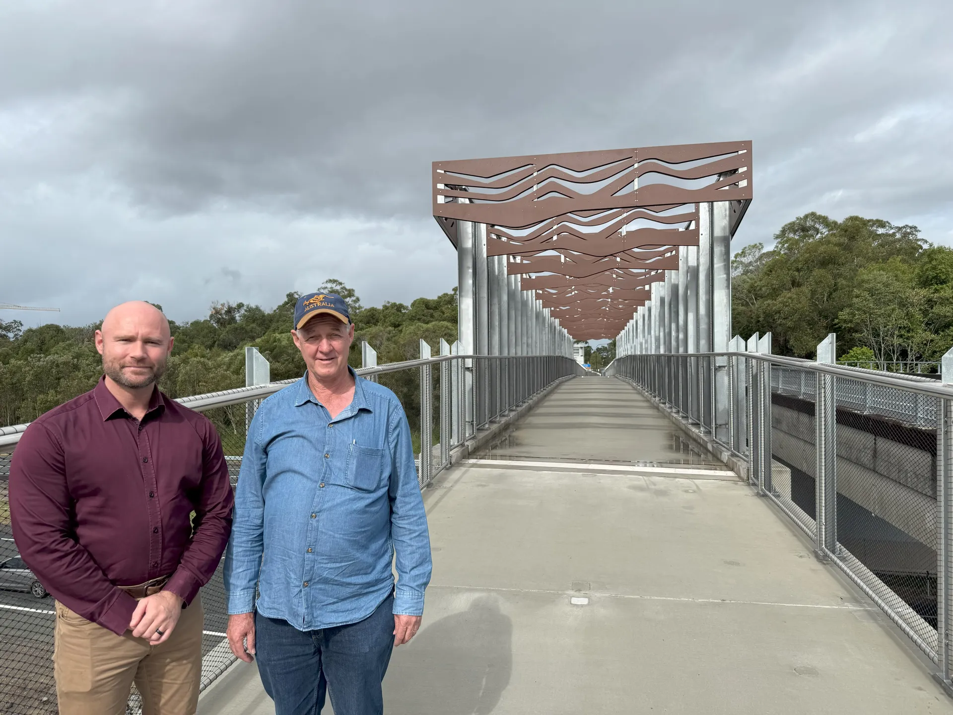 Left to right Cr Dickson in burgundy button down long sleeved shirt and Cr Hungerford in a blue button down long sleeve shirt standing on the footpath and the beginning of the bridge opening pathway.