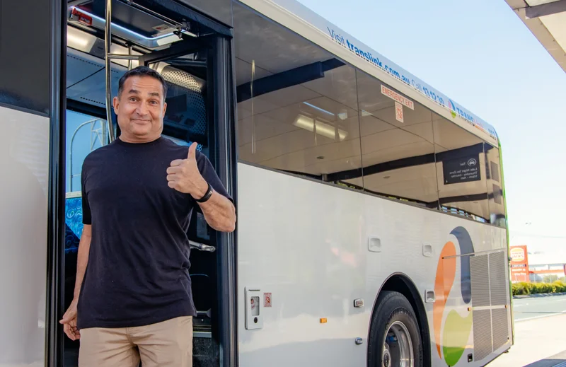 A middle aged, friendly man is getting off a bus at a bus terminal and looking into the camera with a smile while giving a thumb's up.