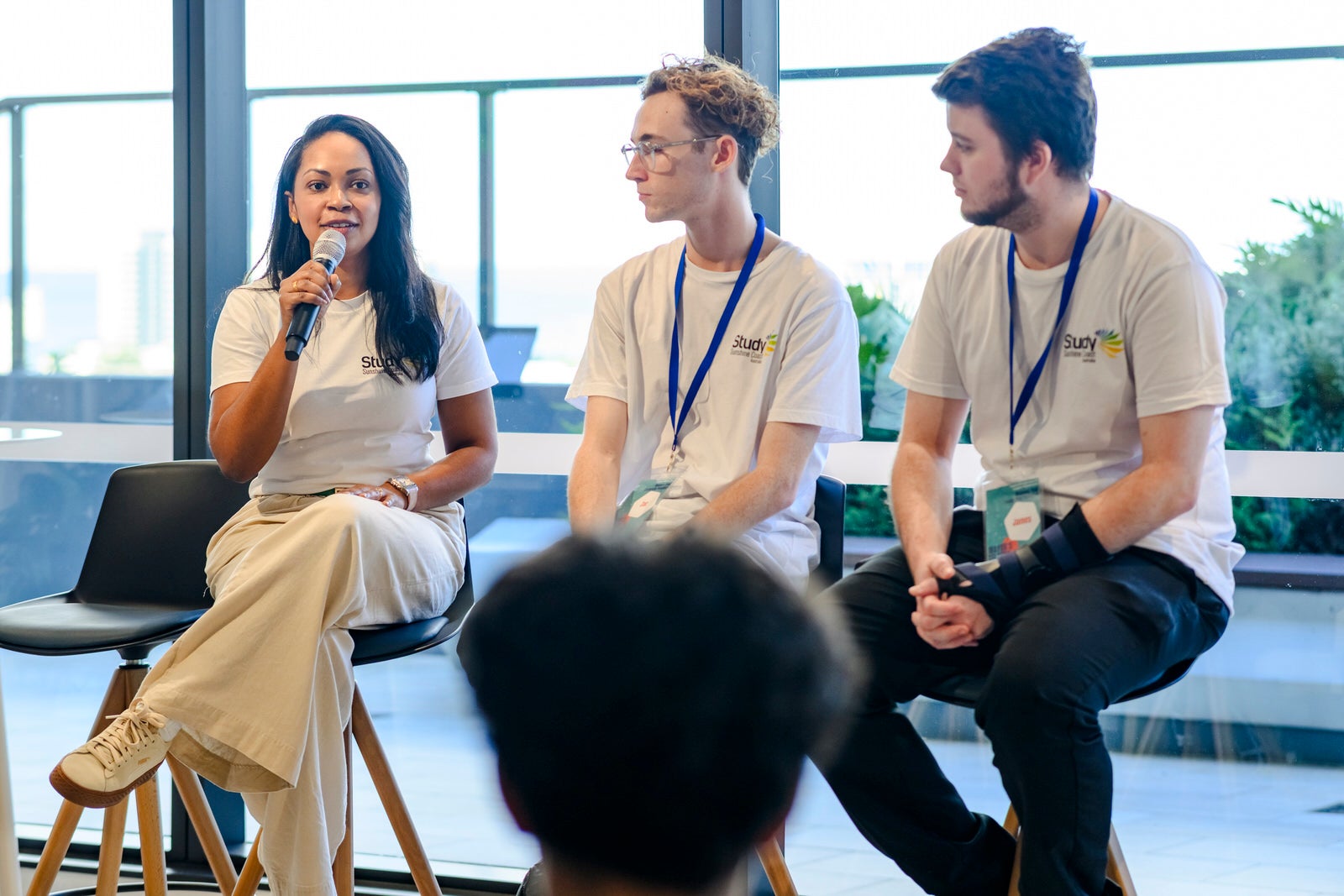 Three speakers, seated, with one person talking on a microphone.