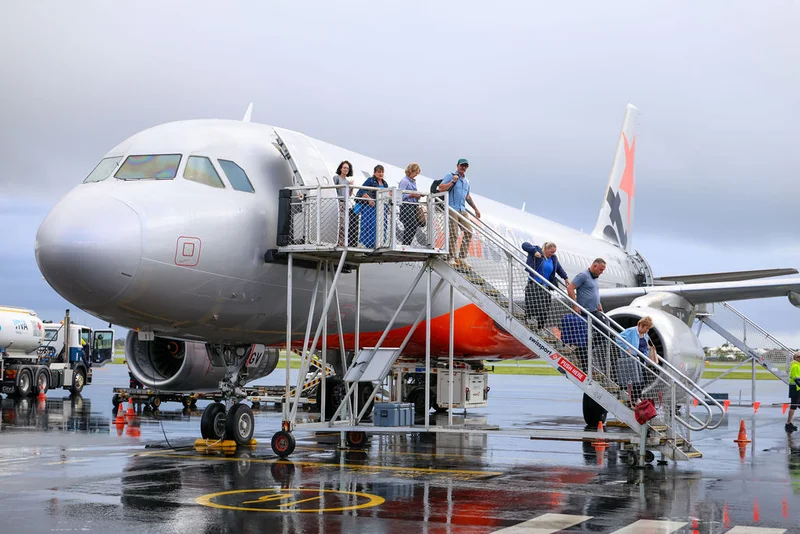 Jestar plane on the tarmac with passengers existing the aircraft via the forward door stairs