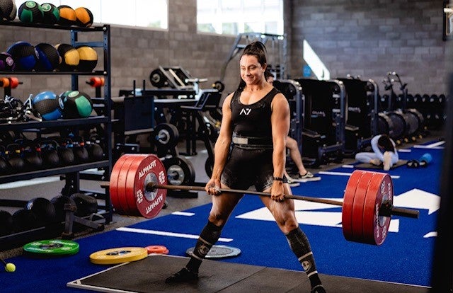 Strong muscular weight lifting woman holding very heavy dumb bells in a gym filled with equipment. 