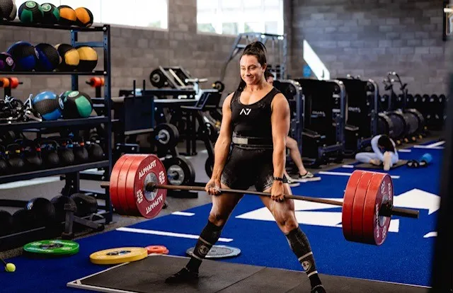 Strong muscular weight lifting woman holding very heavy dumb bells in a gym filled with equipment.